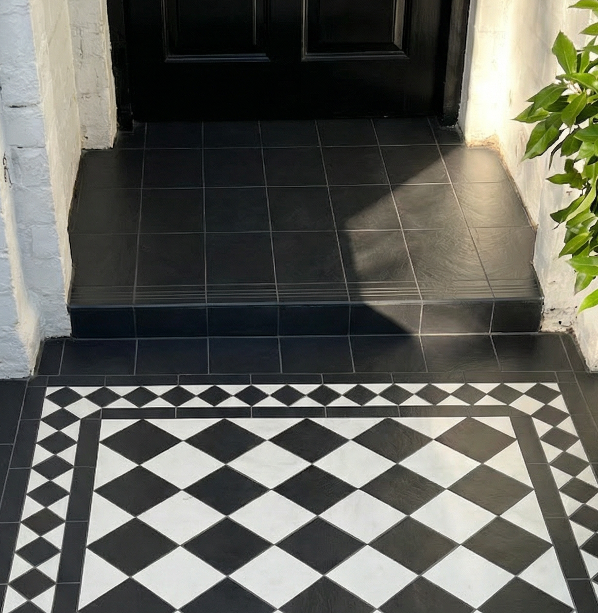 Black and white checkered floor pattern in a hallway with a black door and green plant.