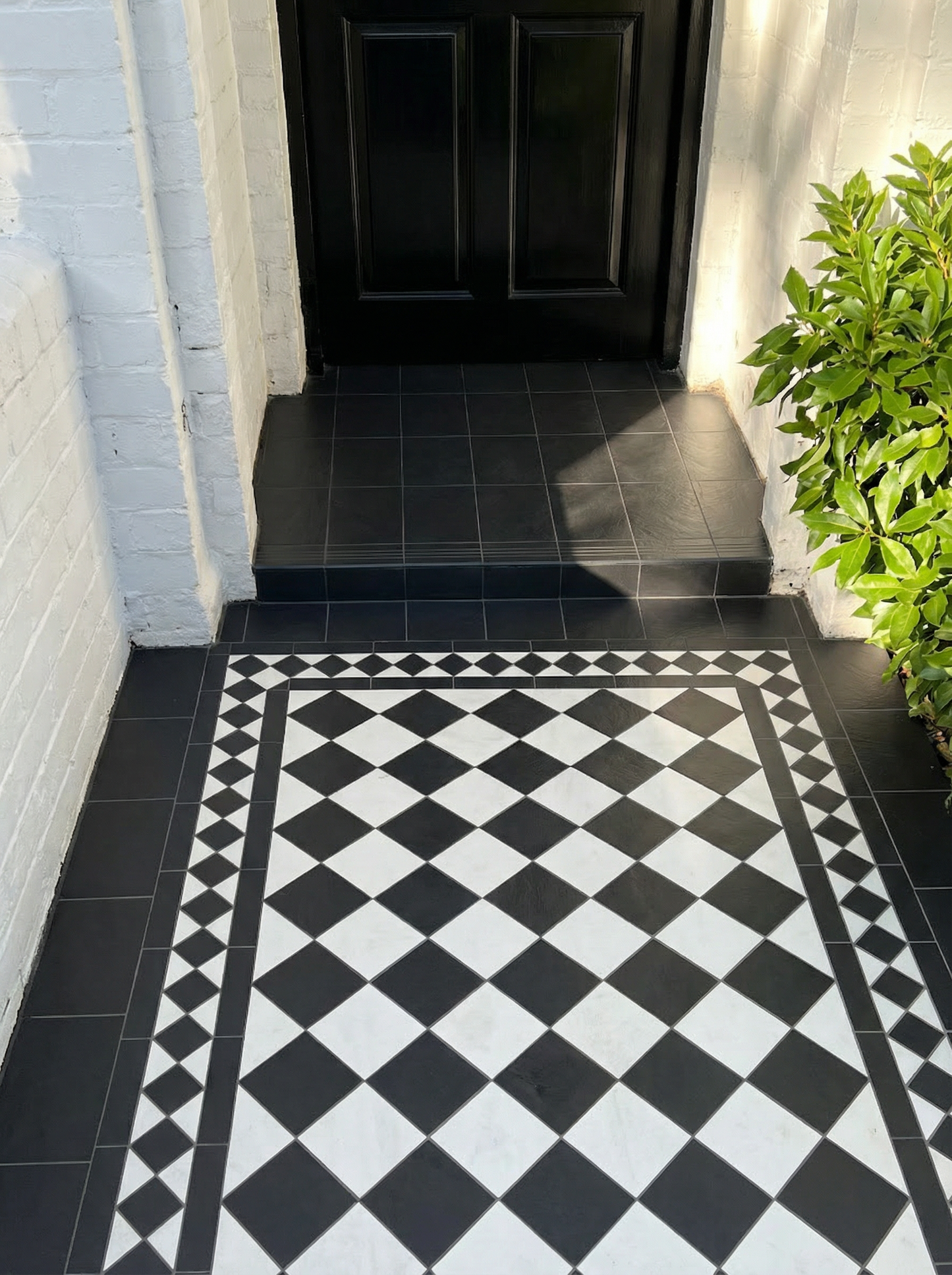 Black and white checkered floor pattern in a hallway with a black door and green plant.